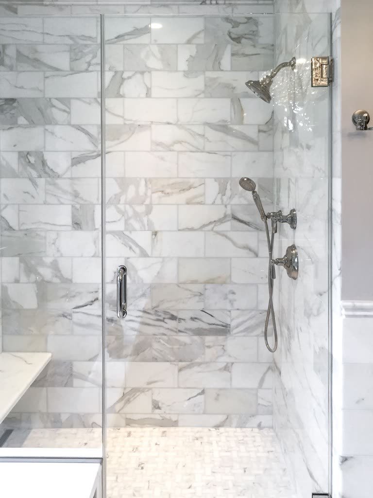 A shower wall built from rectangular Calacatta marble tiles, with a grid of grout joints running between every tile.