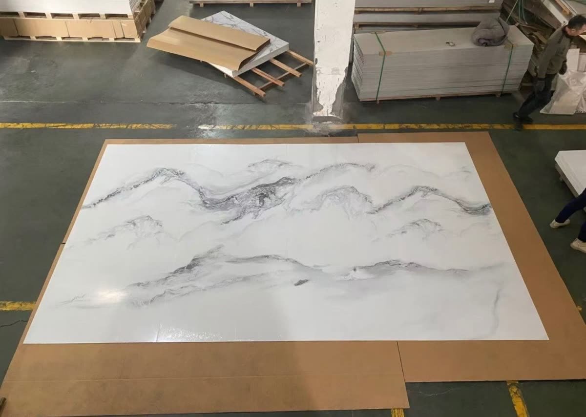 A single marble-look panel laid flat on a warehouse floor, wider than a person is tall, with its veining running unbroken from edge to edge.